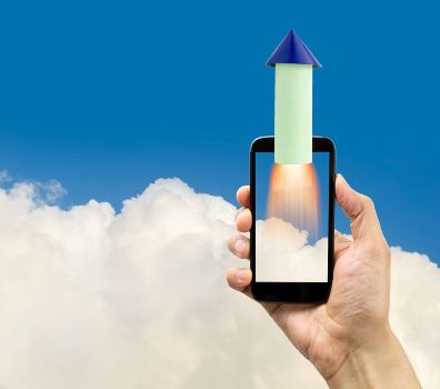 A hand of a man holding a smartphone with a rocket going up with sky full of clouds background